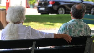 An elderly couple sits on a park bench